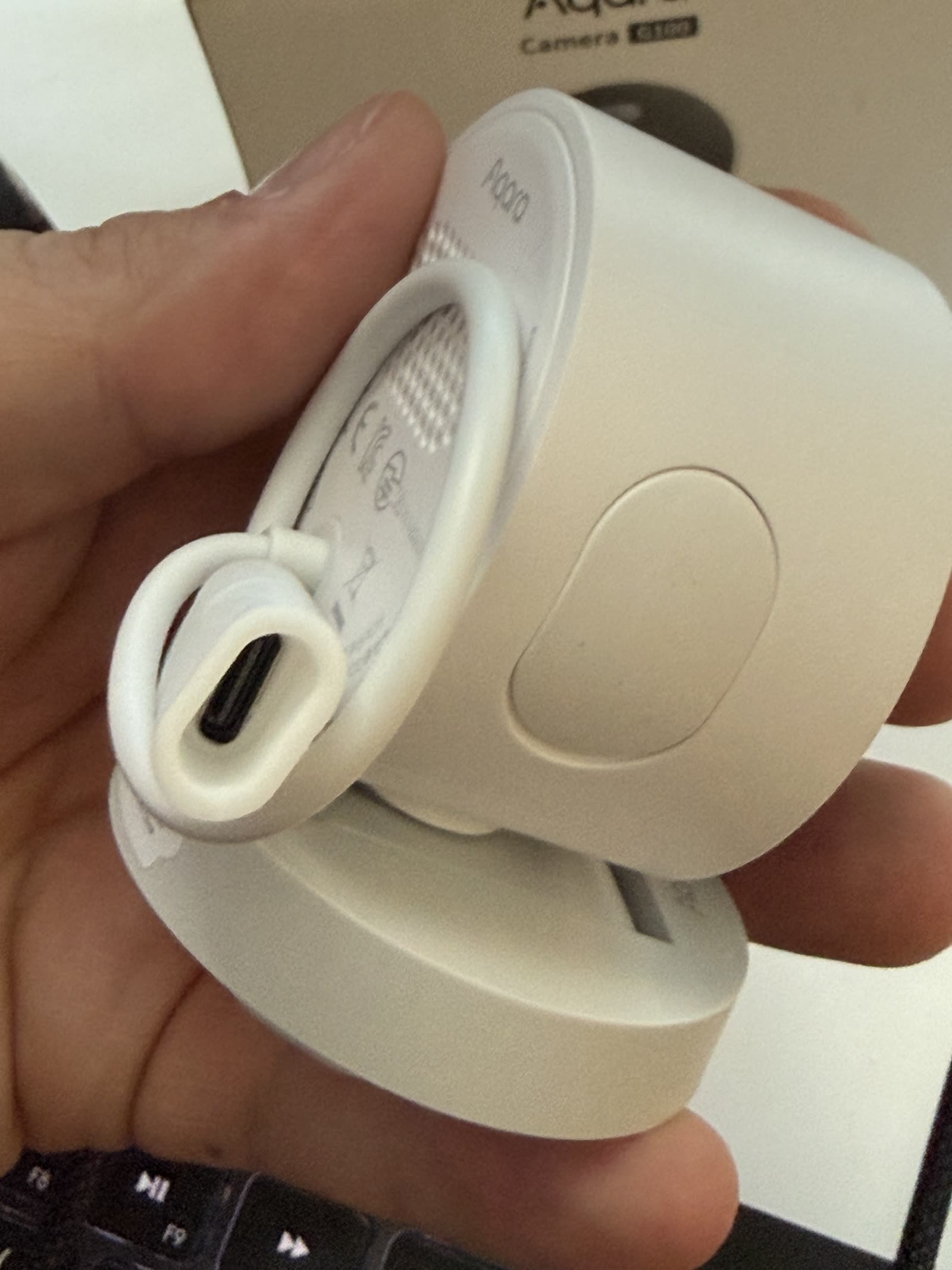 The bottom of the Aqara G100 held in a hand, showing the USB-C plug seated inside a white silicone sealing sleeve.