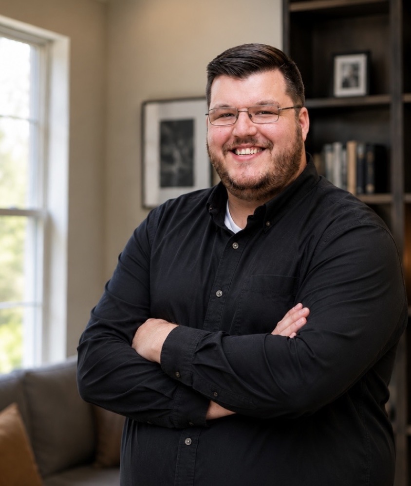 Matthew Easterday, smiling with arms crossed in front of a bookshelf
