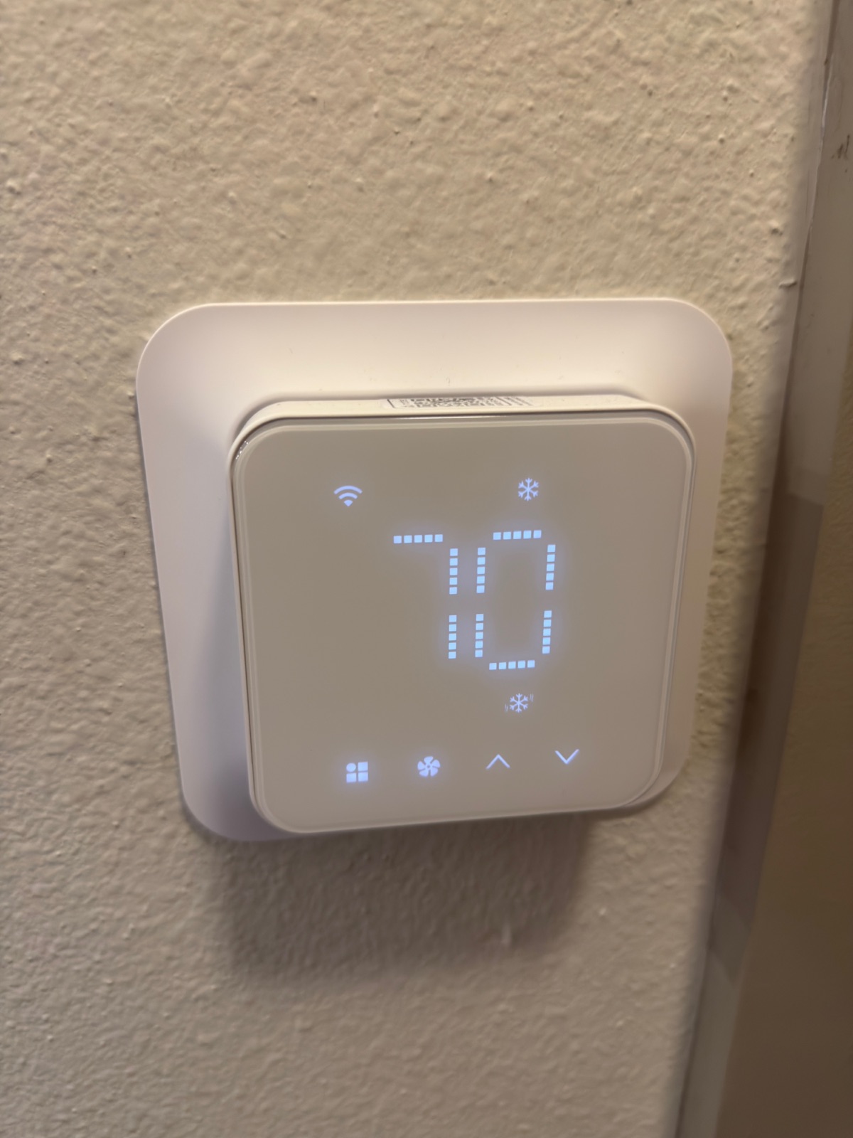 Close-up of the Meross thermostat display showing 70 degrees, a Wi-Fi glyph, a snowflake cooling indicator, and touch controls for mode, fan, up and down.
